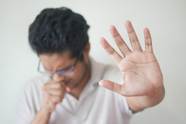 Man coughing and holding up his hand to keep people away.