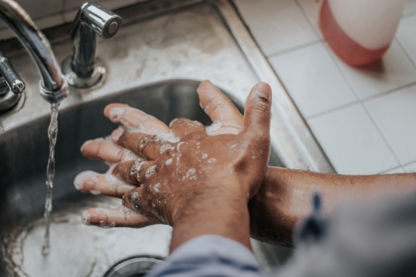 Person washing their hands under a faucet.