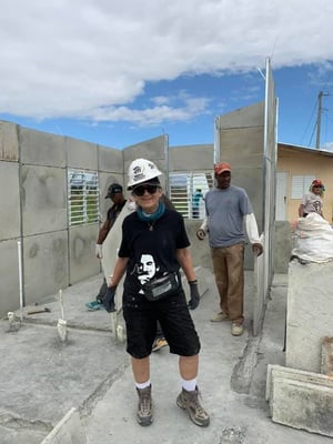 Mary Bolkcom posing in the middle of a partially-finished concrete house, with volunteers behind her.