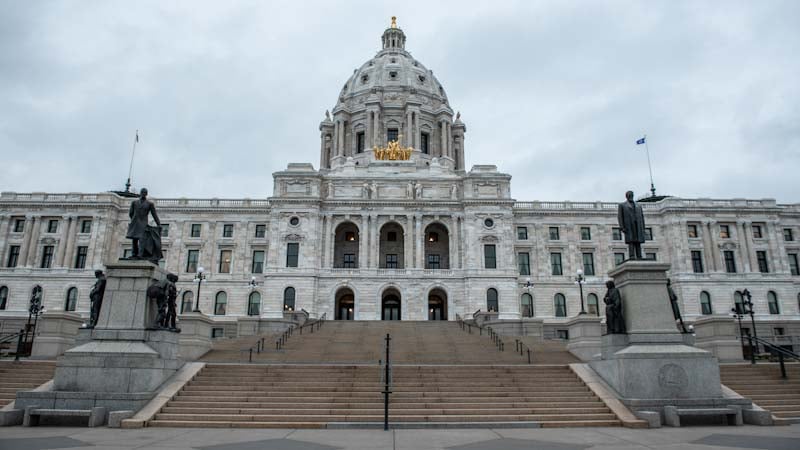 The front of the Minnesota State Capitol building on a cloudy day, looking up the steps in front of the two main statues.
