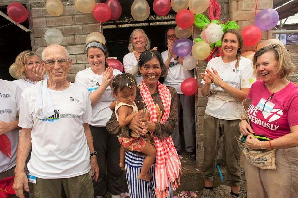 Orin and the other Habitat volunteers at the house dedication in Cambodia. They are standing with the mother and daughter who will now live in the home. Everyone is smiling. 