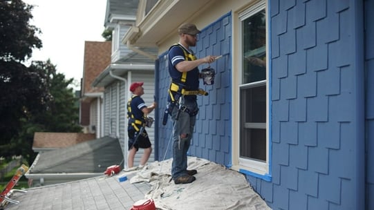 A volunteer painting siding of a house.