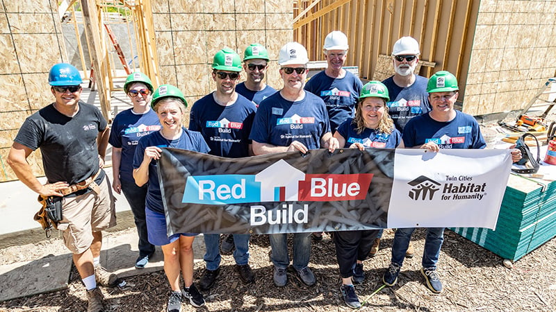 Group of volunteers on a build site holding a Red Blue Build banner