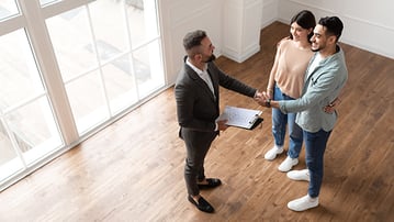 Man and woman shaking hands with realtor inside an empty home.