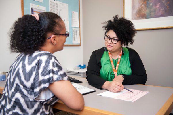 A woman going over paperwork with another woman across from her desk.