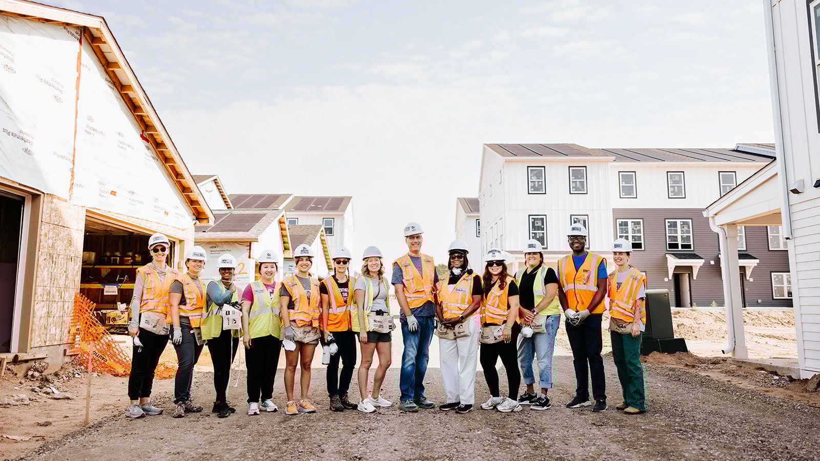 A large group of people in hard hats and safety vests stand on a construction site