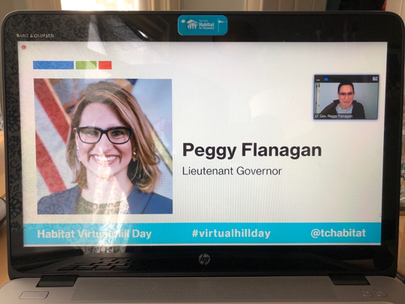 An HP computer screen showing a Zoom presentation with a small window showing the presenter. The Zoom slide features an image of Lieutenant Governor Peggy Flanagan smiling in a black shirt and blue jacket in front of the American flag. There are three stylized rectangles above the image in bright blue, bright green, and orange. A bright blue bar at the bottom of the screen says "Habitat Virtual Hill Day, #VirtualHillDay," and "@TCHabitat"