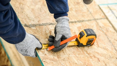 A person marking measurements on a sheet of wood.