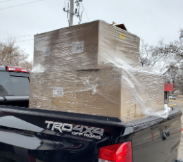 A black truck carrying several boxes full of masks down the road.