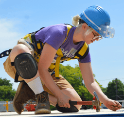 Woman in safety gear volunteering to build a house on a Twin Cities Habitat for Humanity home build site, Using a hammer to pound in a nail-