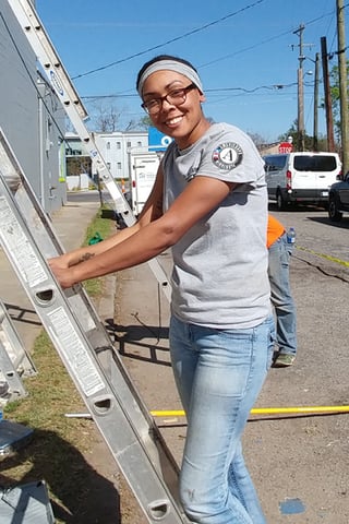 AmeriCorps volunteer steadying a ladder.