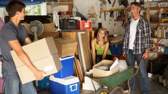 A smiling family moving boxes in a garage.