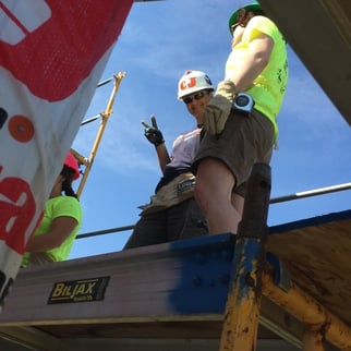 CJ Fitzsimmons giving a peace sign next to some volunteers on a construction platform.