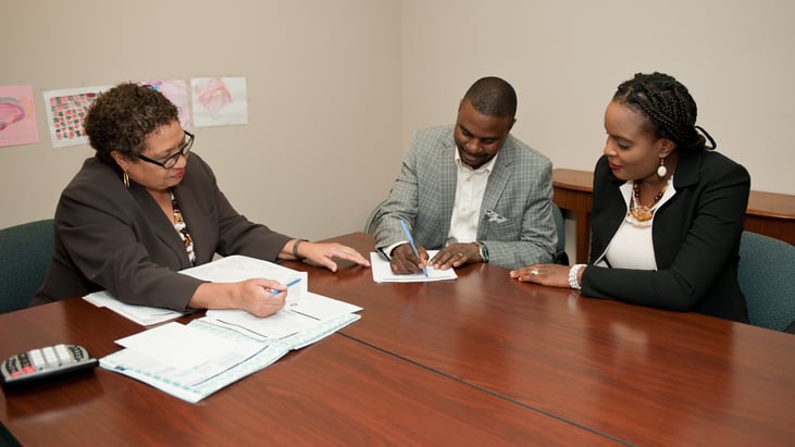 Fred and Brigitte signing papers with their financial coach, Linda White, at Model Cities.