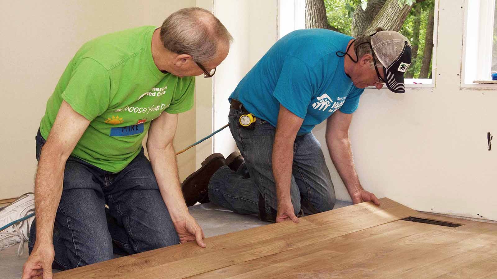 Chris learning to install flooring from a Holy Hammers volunteer