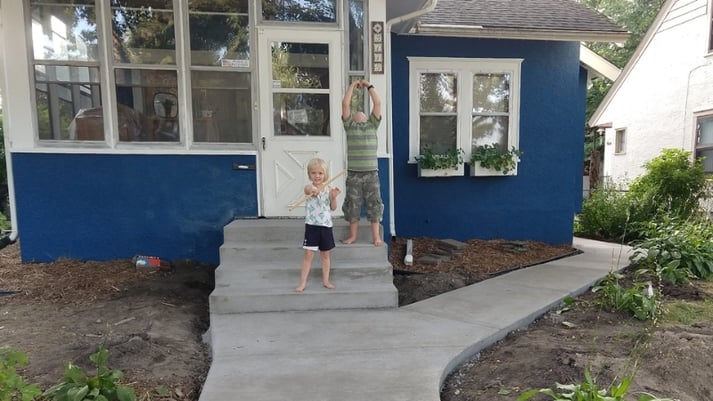 The kids in front of the repaired home with new blue paint and window boxes.