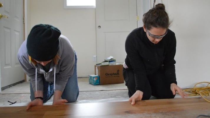 AmeriCorps members laying down flooring.