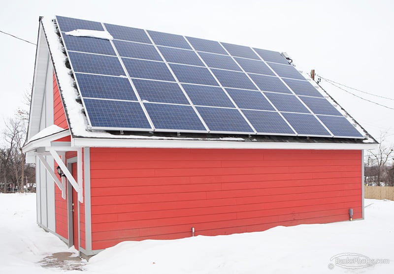 A bright red shed in the snow, with solar panels on the roof.