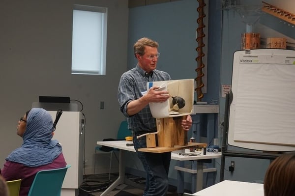 Steve showing the back of an exposed toilet tank to explain the parts.