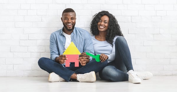 Young black home buyer couple holding papercraft home and key.