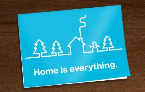 card for tribute gifts in blue, with white text saying "Home is everything." A white line drawing of a winter landscape with trees, a house, and a snowman is above the text.