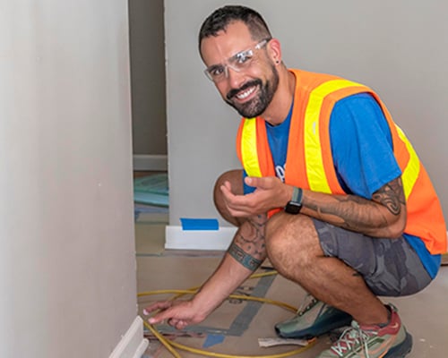 A bearded person wearing a safety vest and goggles painting trim.