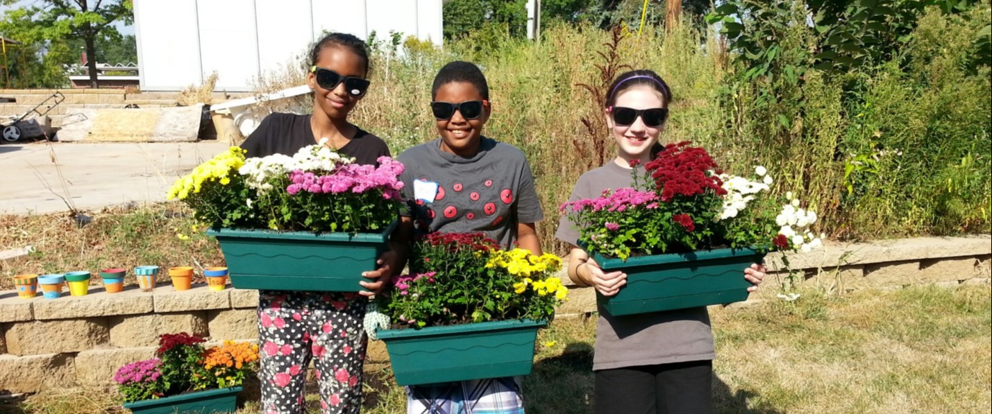 Three youth landscape volunteers holding planter boxes with flowers