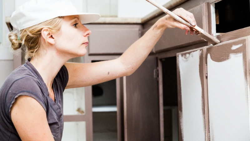 A person with long blond hair painting cabinets.