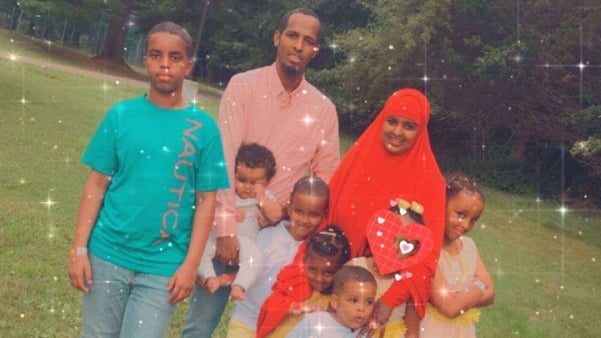Mohamed, his wife Safia, and their six children stand smiling in a park.