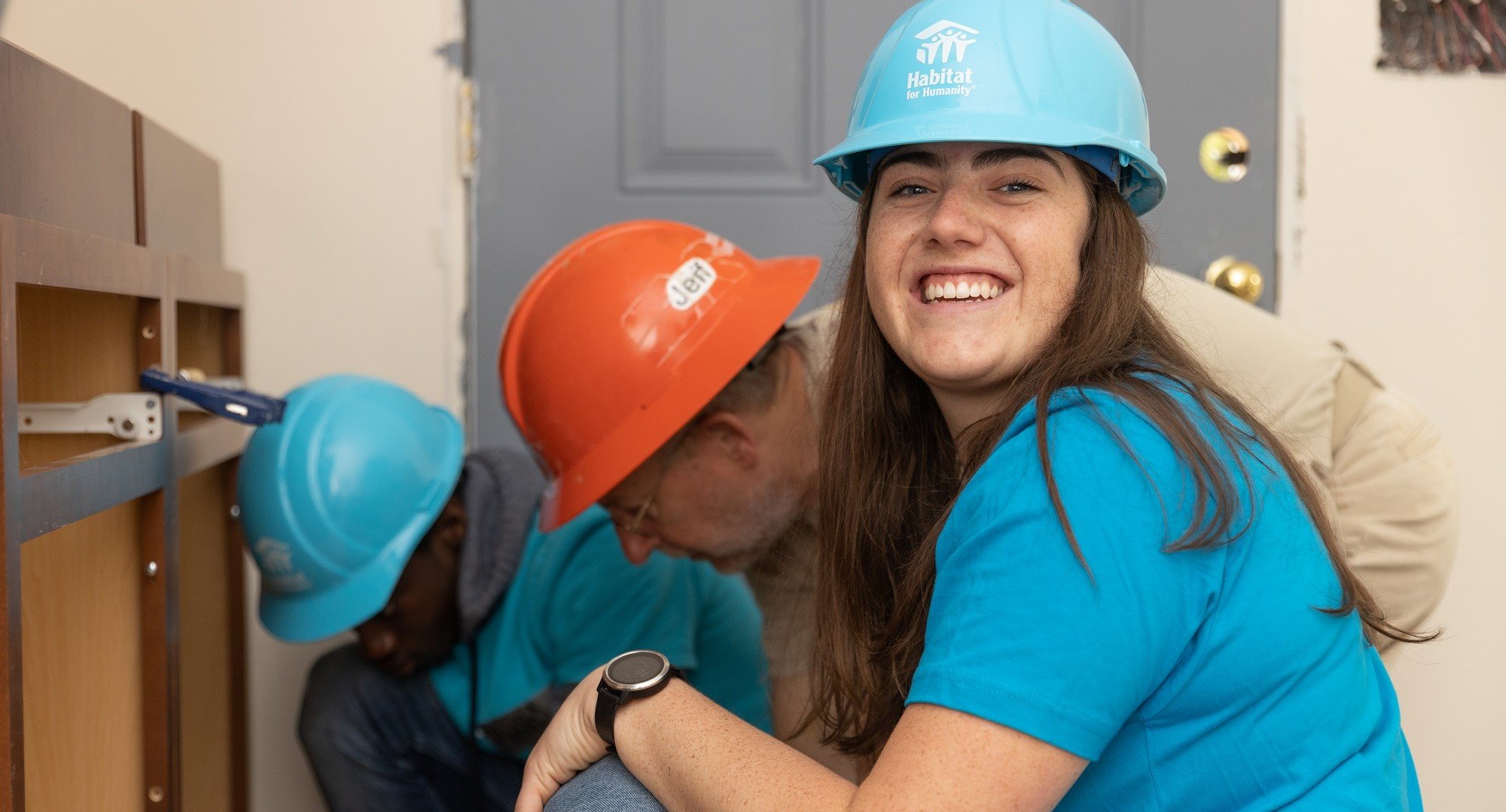 Volunteering working on cabinet and smiling.