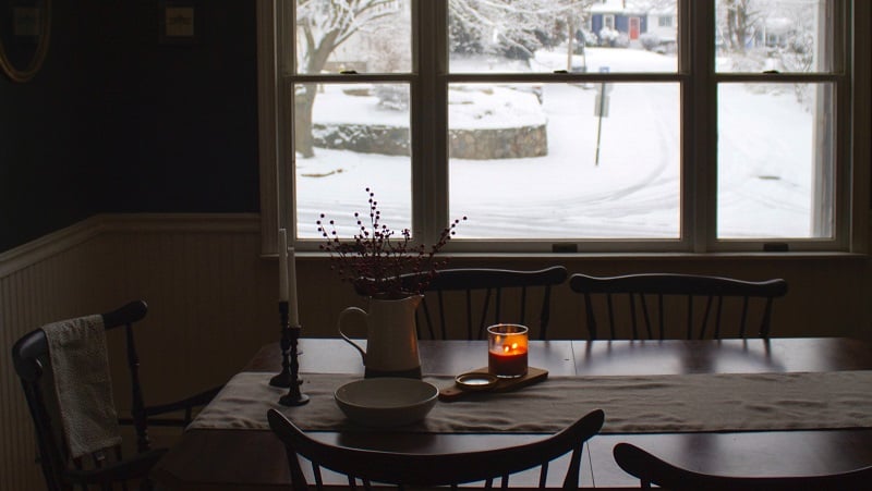 A candle-lit dining room with a snowy view of a street.