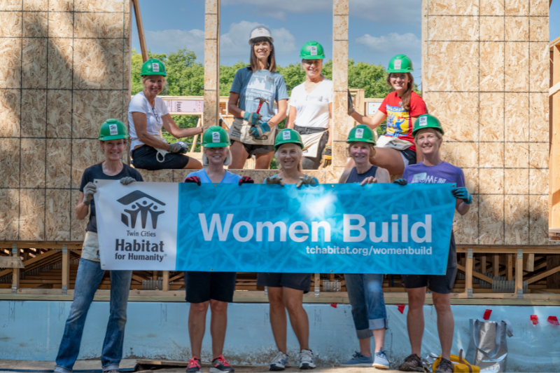 Several people in hard hats holding the Women Build banner.