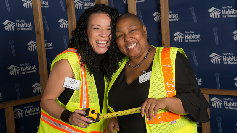 Two HHBT attendees in safety vests, holding an extended tape measure.