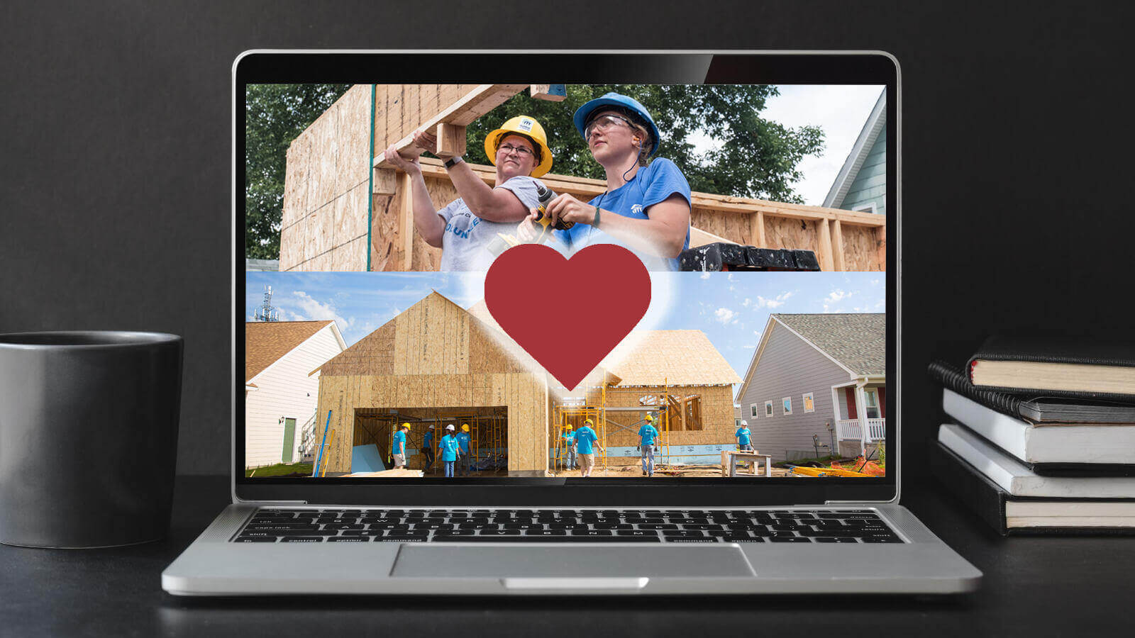 Against a dark gray background, a laptop on a desk next to a pile of books on the right and a cup on the left. The laptop displays a red heart over images of volunteers at build sites.