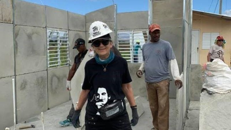 Mary Bolkcom posing in the middle of a partially-finished concrete house, with volunteers behind her.