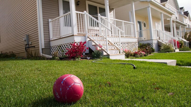 A beige house with a front yard. A red soccer ball sits on the front yard.