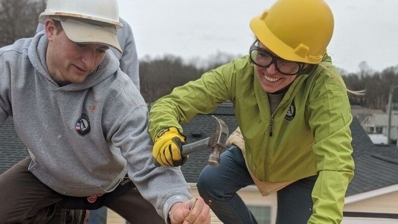 Two AmeriCorps members working together on a roof.
