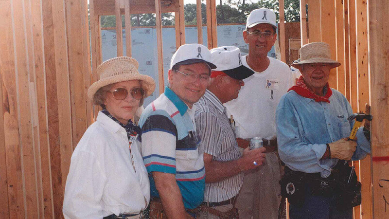 Kenny posing with President Jimmy Carter and two other volunteers inside of a partially-framed house.