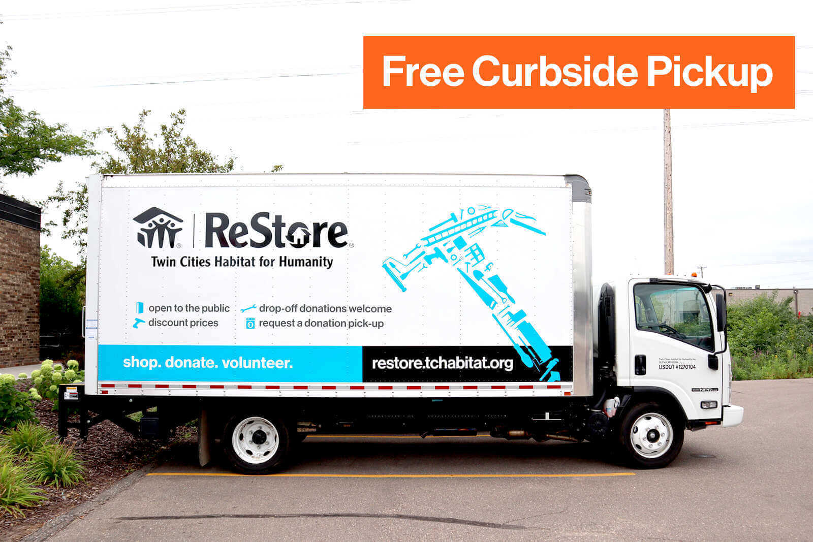 Outside on a parking lot sits a white truck that has the ReStore logo, a large light blue hammer made up of many tools, a blue bar at the bottom that says 