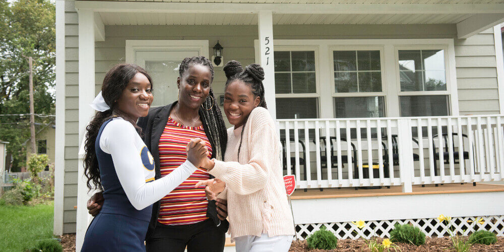 LeAndra and her two children smiling in front of their house.