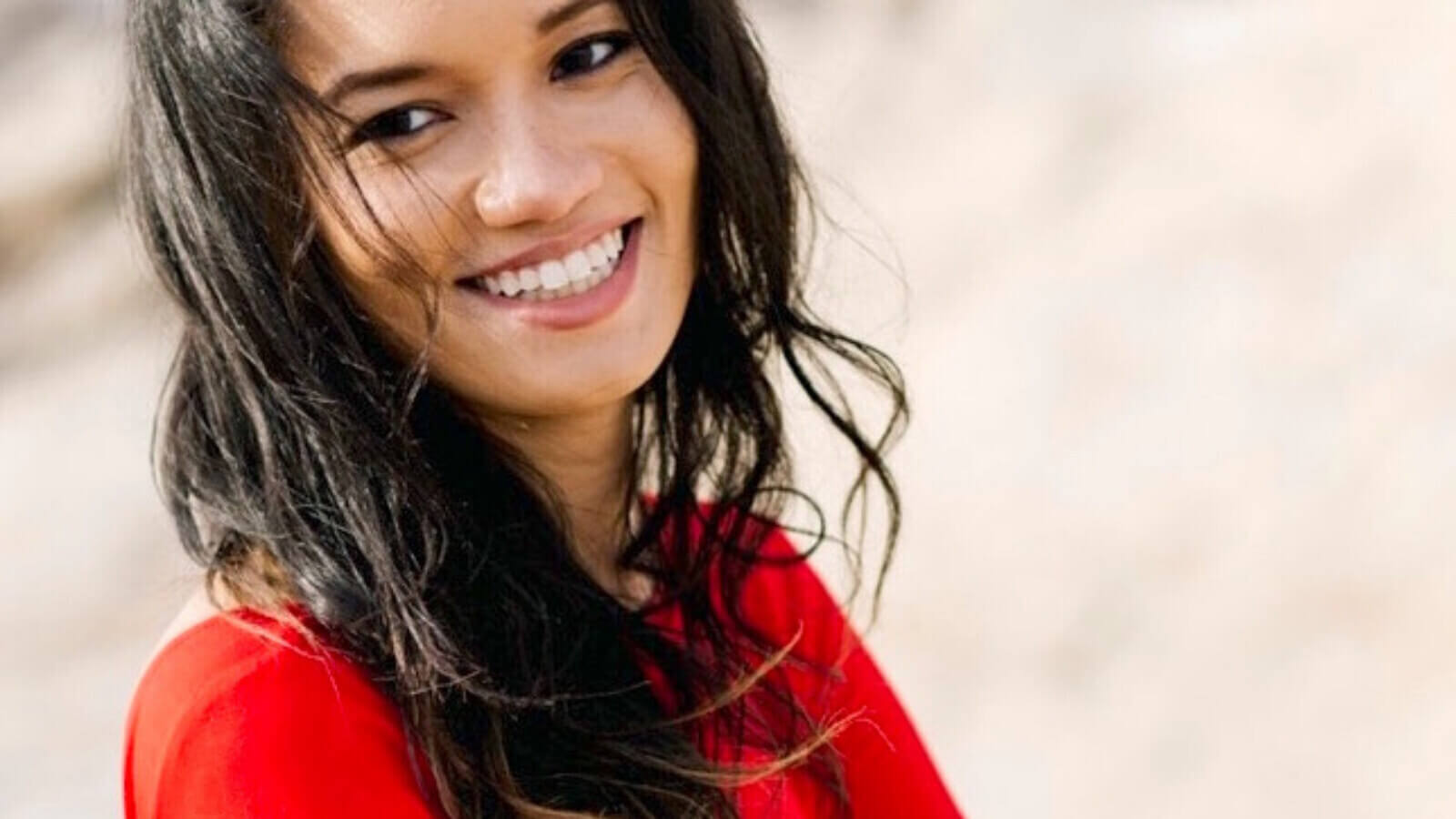 Josie Duffy Rice, in a bright red sweater, smiling with her arms crossed.