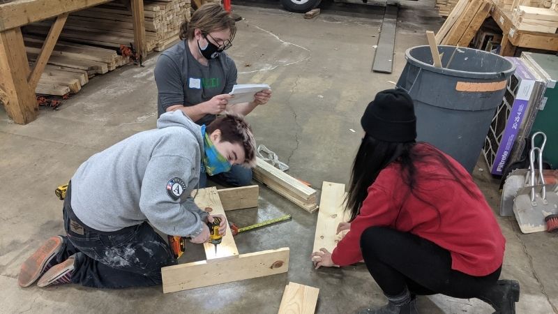 AmeriCorps members building frames in a warehouse.
