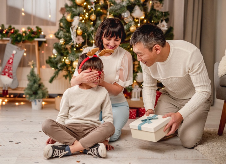 family of three in front of a tree getting ready to open presents