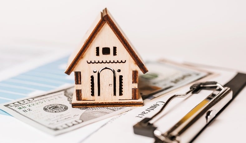 Wooden house on clipboard and money 