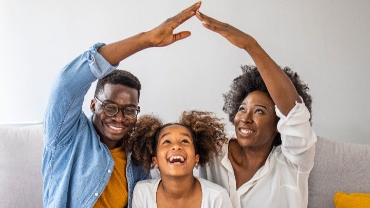 Mom and dad with their young child between them, and the parents are making a roof with their arms