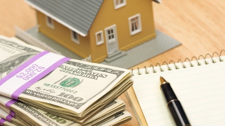 Miniature house next to a stack of money and a pen and paper.