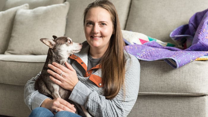 Lindsay holding her Chihuahua Lily in front of her couch in her home.