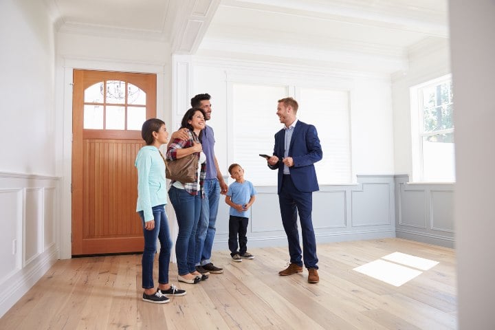 Mom, dad, and kids talking with a realtor inside an empty front room