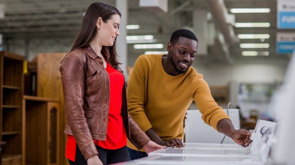 Two people looking at a price tag on a washing machine.