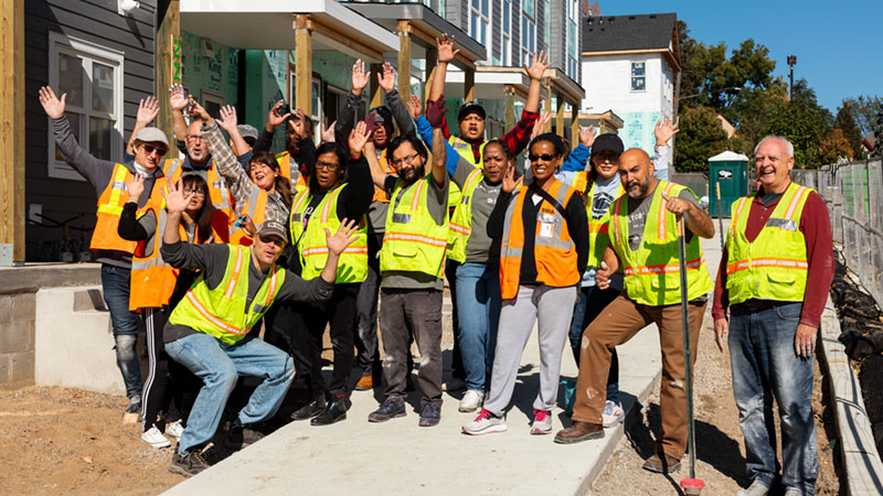 Volunteers in construction safety gear celebrating with their arms in the air.